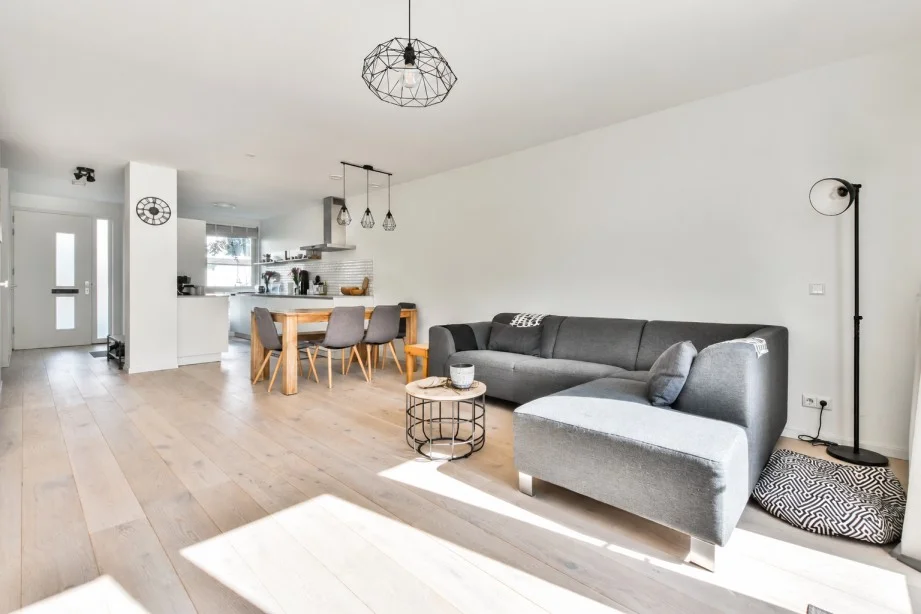 Open-plan house interior with grey sectional sofa, dining area and modern kitchen